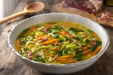 Sopa juliana de verduras con jamón servida en plato hondo, con zanahoria, repollo y espinacas en tiras finas