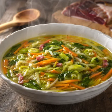 Sopa juliana de verduras con jamón servida en plato hondo, con zanahoria, repollo y espinacas en tiras finas