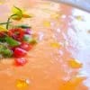 Plato de salmorejo cordobés espeso con picadillo de pimiento y una flor de tomatera, con gotas de aceite de oliva por encima