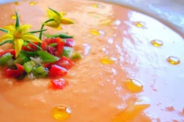 Plato de salmorejo cordobés espeso con picadillo de pimiento y una flor de tomatera, con gotas de aceite de oliva por encima