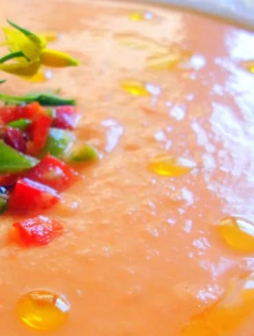 Plato de salmorejo cordobés espeso con picadillo de pimiento y una flor de tomatera, con gotas de aceite de oliva por encima