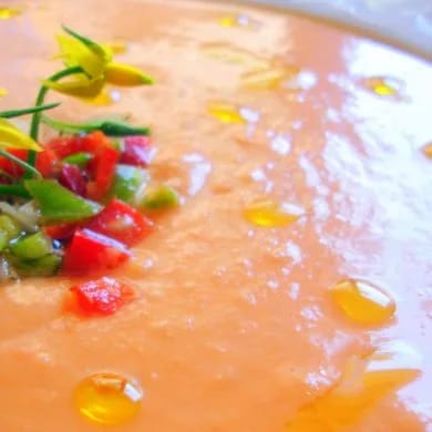 Plato de salmorejo cordobés espeso con picadillo de pimiento y una flor de tomatera, con gotas de aceite de oliva por encima