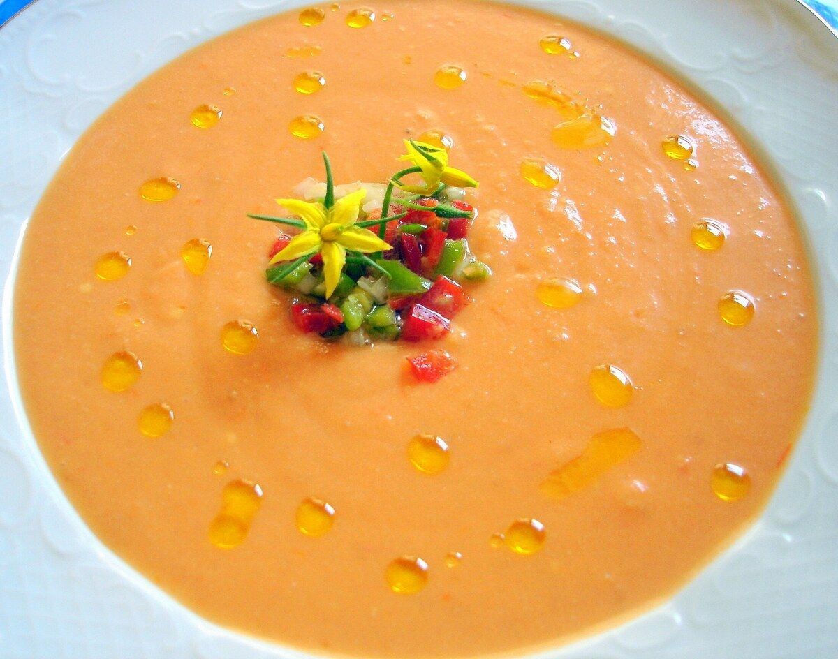 Salmorejo cordobés cremoso y anaranjado con un hilo de aceite de oliva virgen extra y guarnición de verduras