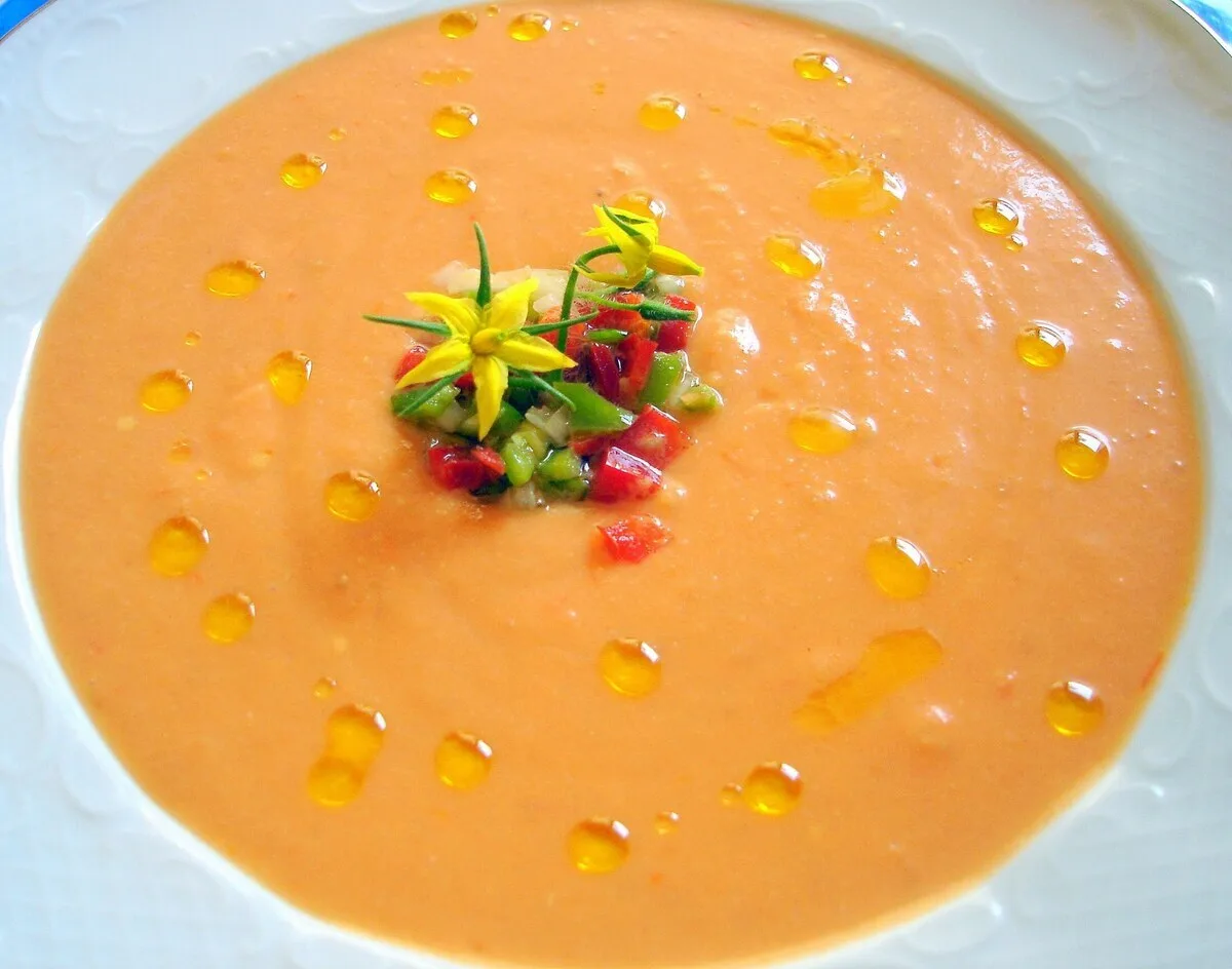 Salmorejo cordobés cremoso y anaranjado con un hilo de aceite de oliva virgen extra y guarnición de verduras