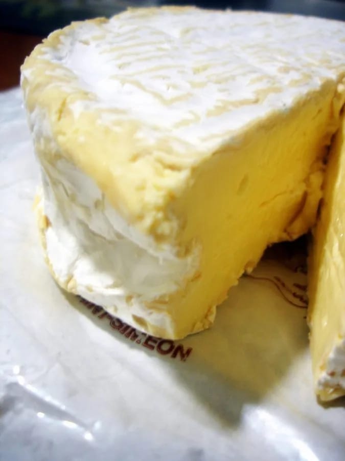 Queso coulommiers de leche cruda comprado en un mercado de París, abierto sobre su papel de envolver, con la pasta cremosa a la vista