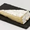 Cuña de queso brie con su corteza florecida blanca y la pasta cremosa, sobre una tabla de pizarra negra