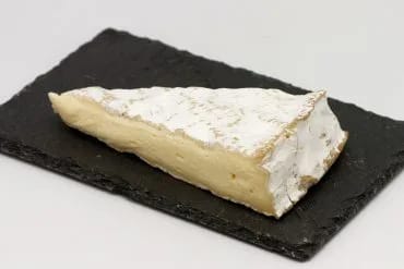Cuña de queso brie con su corteza florecida blanca y la pasta cremosa, sobre una tabla de pizarra negra