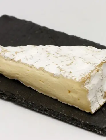 Cuña de queso brie con su corteza florecida blanca y la pasta cremosa, sobre una tabla de pizarra negra