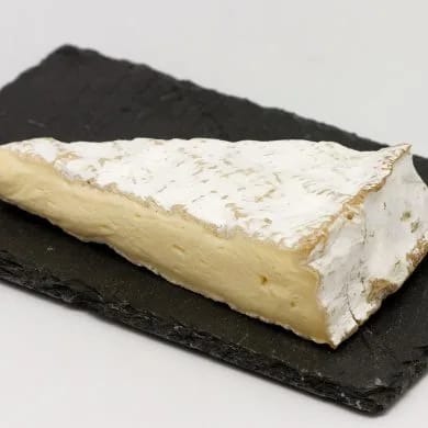 Cuña de queso brie con su corteza florecida blanca y la pasta cremosa, sobre una tabla de pizarra negra
