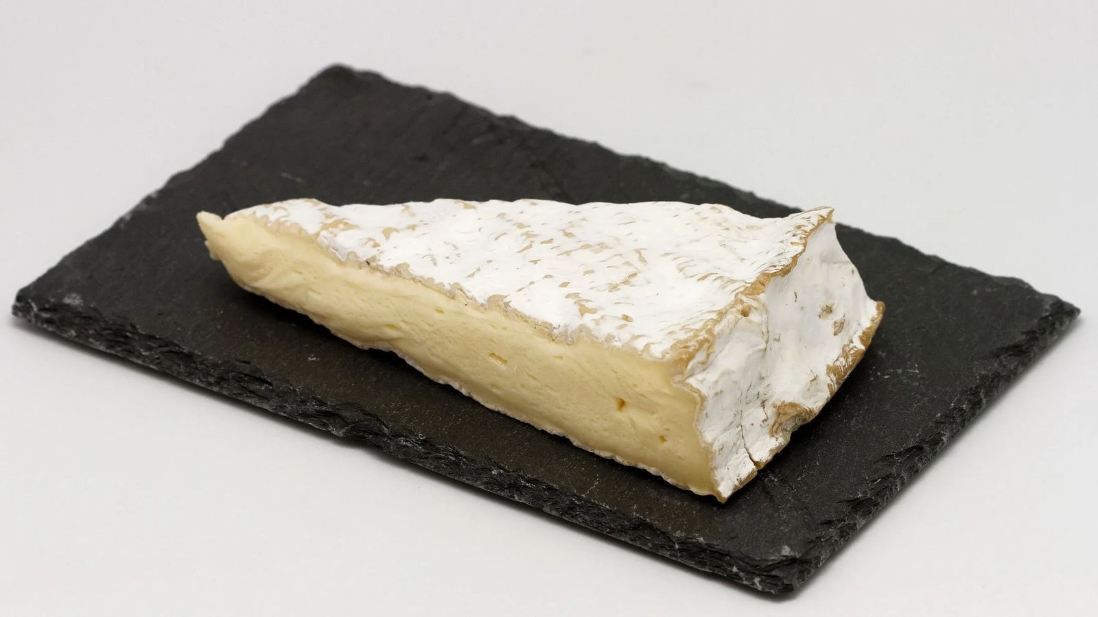 Cuña de queso brie con su corteza florecida blanca y la pasta cremosa, sobre una tabla de pizarra negra
