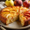 Tarta de manzana y melocotón casera con rodajas de fruta en abanico doradas y un trozo cortado que deja ver la miga jugosa, sobre una mesa de madera