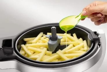 Una cucharada de aceite vertida sobre las patatas crudas cortadas en bastones dentro de la cubeta de la ActiFry