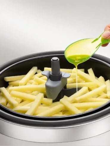 Una cucharada de aceite vertida sobre las patatas crudas cortadas en bastones dentro de la cubeta de la ActiFry