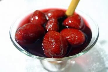 Fresas al vino tinto servidas en copa de cristal con una rama de canela