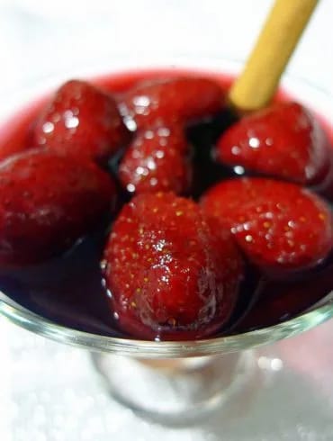 Fresas al vino tinto servidas en copa de cristal con una rama de canela