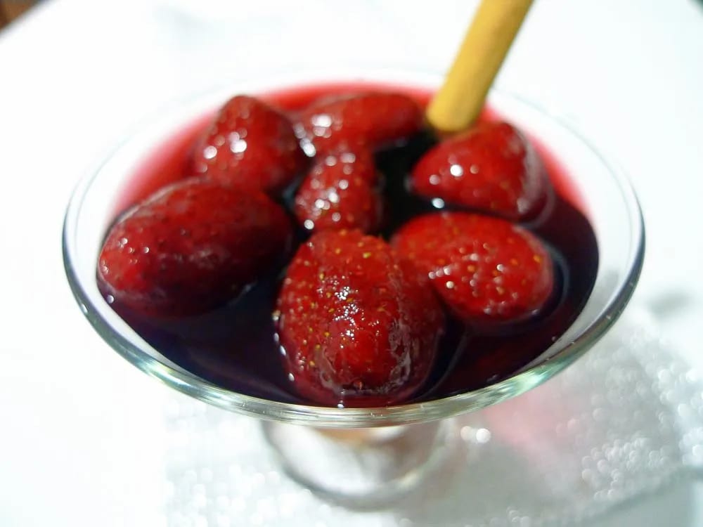 Fresas al vino tinto servidas en copa de cristal con una rama de canela
