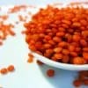Lentejas rojas crudas en un cuenco blanco, con su color naranja intenso y algunos granos sueltos alrededor