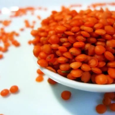 Lentejas rojas crudas en un cuenco blanco, con su color naranja intenso y algunos granos sueltos alrededor