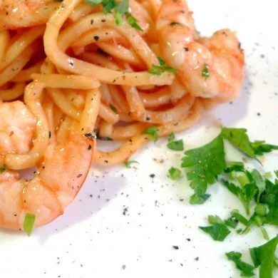 Espaguetis con langostinos servidos en plato blanco con perejil picado y pimienta negra recién molida