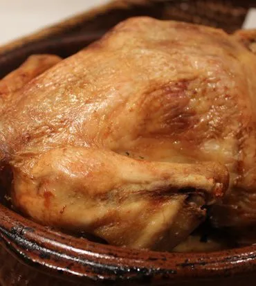 Pollo al horno tradicional dorado en cazuela de barro con su jugo
