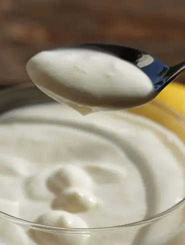 Cucharada de mousse de limón cremosa sobre una copa de cristal, con limones al fondo