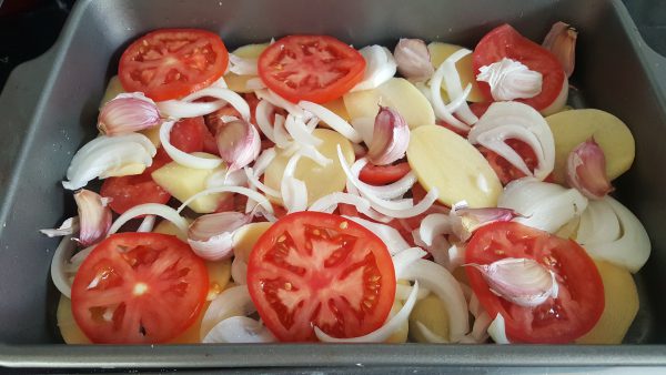 Cortamos en rodajas no muy gruesas el tomate y la cebolleta. Colocamos encima de la patata.