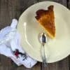 Ración entera de tarta de queso y mango con la mermelada brillante por encima, sobre un plato claro con una servilleta bordada