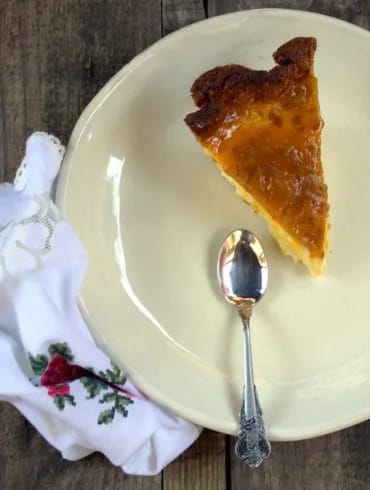 Ración entera de tarta de queso y mango con la mermelada brillante por encima, sobre un plato claro con una servilleta bordada