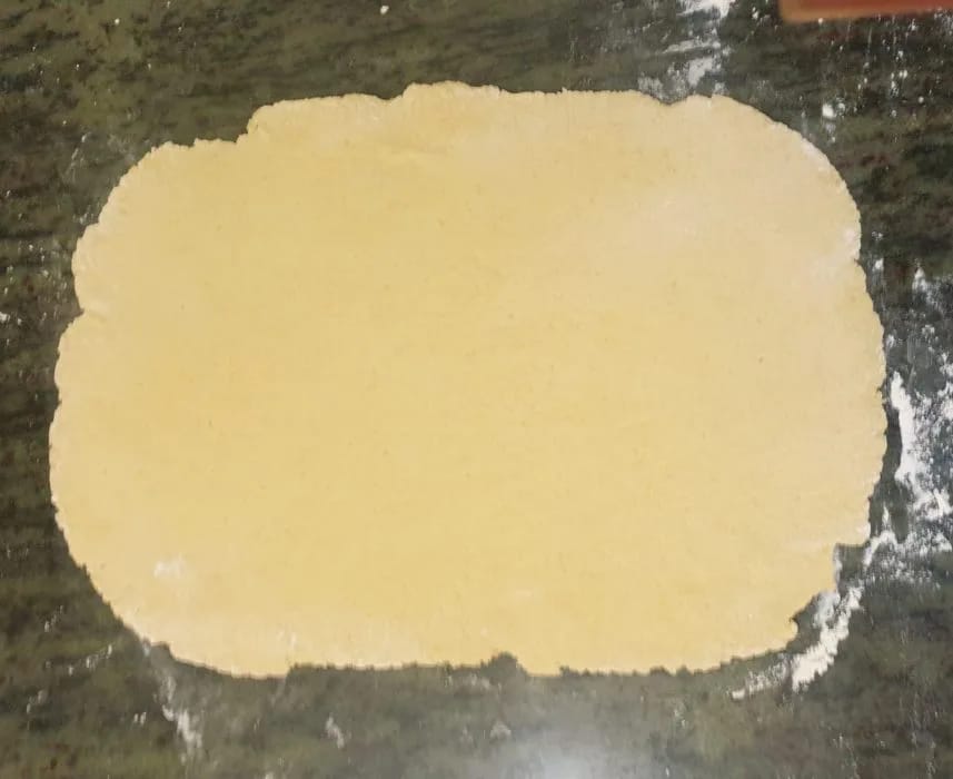 Masa de los rollos de canela extendida en un rectángulo con el rodillo sobre la mesa enharinada