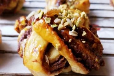 Rollo de canela sueco en forma de nudo con azúcar perlado y granillo de pistacho, sobre una rejilla de enfriado