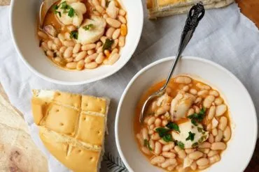 Plato hondo de alubias con carrilleras de bacalao espolvoreadas con perejil, visto de cerca