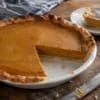 Tarta de calabaza americana con una porción cortada, sobre masa quebrada de borde ondulado y relleno cuajado de color ocre