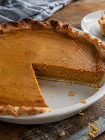 Tarta de calabaza americana con una porción cortada, sobre masa quebrada de borde ondulado y relleno cuajado de color ocre